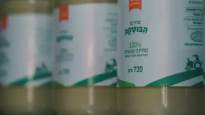 צנצנות טחינה מהמותג חומוס הבוטקה, 100% טחינה טבעית, מונחות על שולחן מבריק.