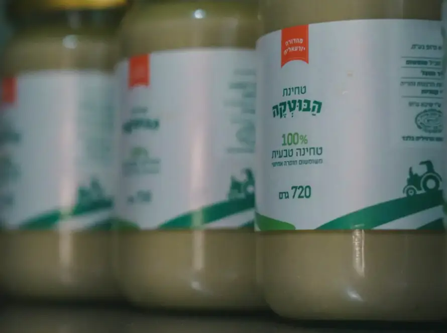 צנצנות טחינה מהמותג חומוס הבוטקה, 100% טחינה טבעית, מונחות על שולחן מבריק.